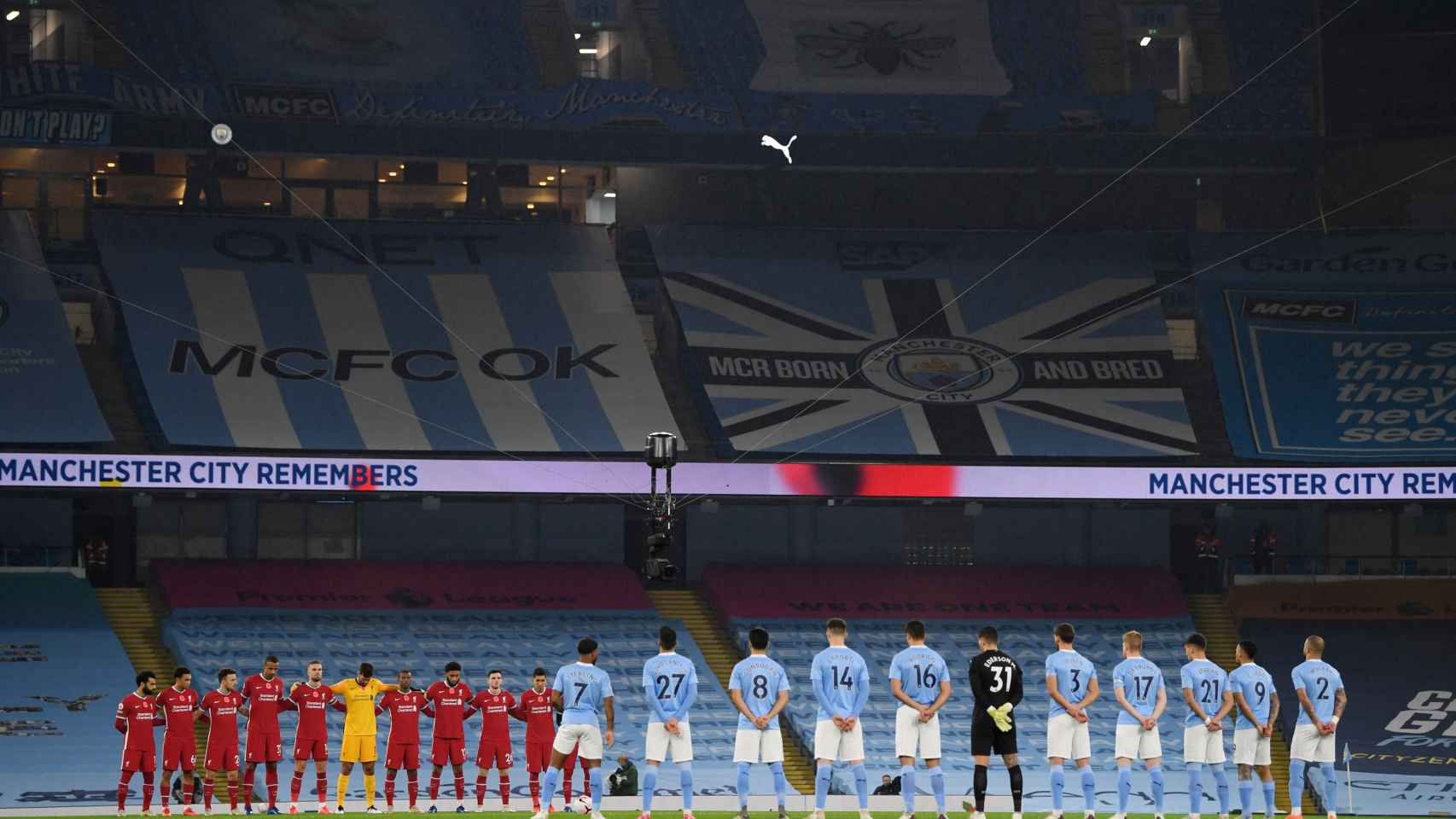 Los jugadores de Liverpool y Manchester City, durante un minuto de silencio en el Etihad Stadium con las gradas vacías