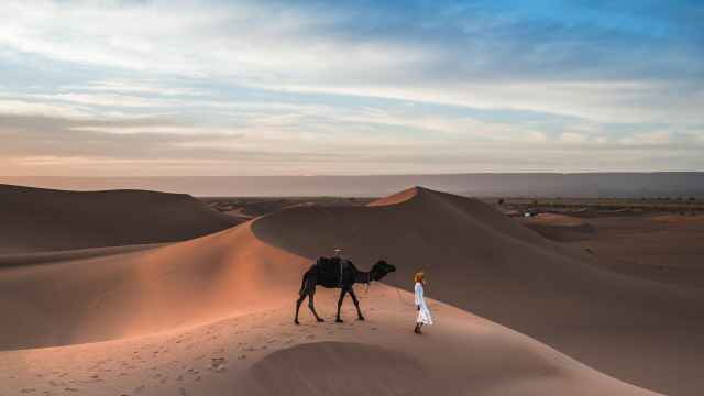 Un camello y una persona pasean por las dunas.