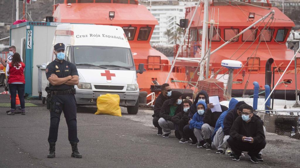 Un policía custodia a un grupo de inmigrantes que espera su traslado fuera del muelle de Arguineguín.