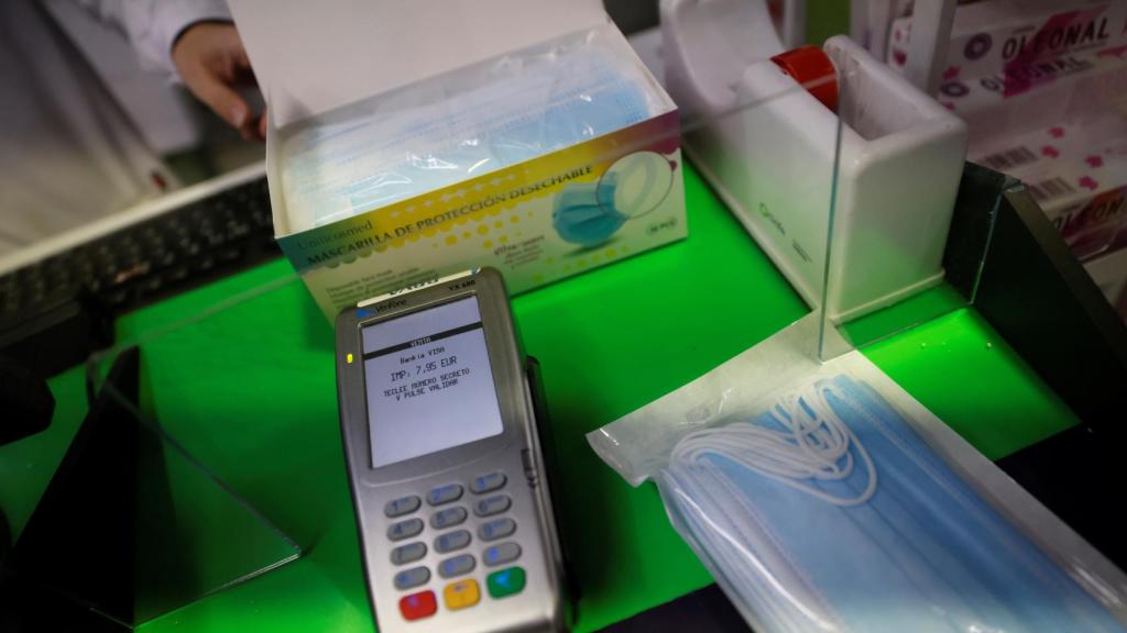 Una persona, pagando con datafono, por un paquete de mascarillas quirúrgicas.