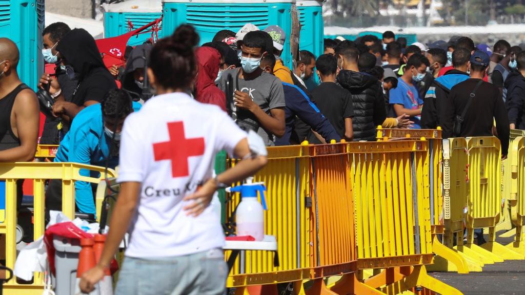 Una voluntaria de la Cruz Roja, junto a decenas de inmigrantes en el muelle de Arguineguín.