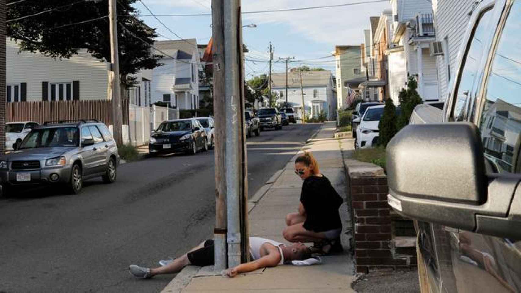 Una mujer se agacha en la acera junto a su novio, que no responde ni respira después de una sobredosis de opioides en un suburbio de Boston.