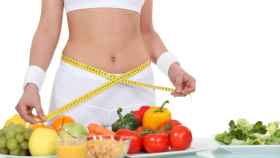 Una mujer mide su vientre frente a una selección de frutas y verduras.
