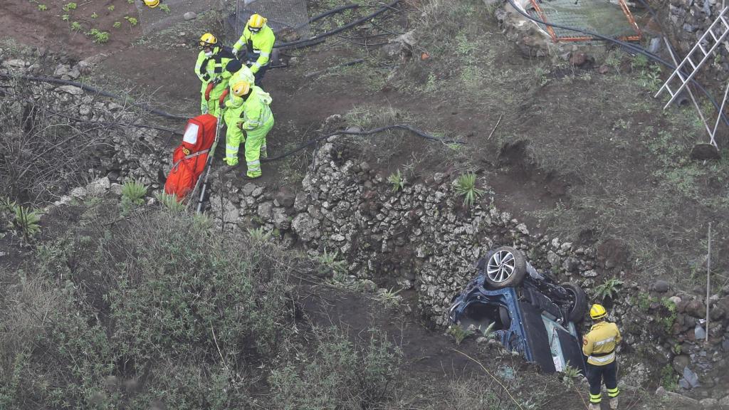 El coche accidentado en la profundidad del barranco y los operarios rescatando los cuerpos.