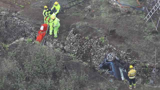 El coche accidentado en la profundidad del barranco y los operarios rescatando los cuerpos.