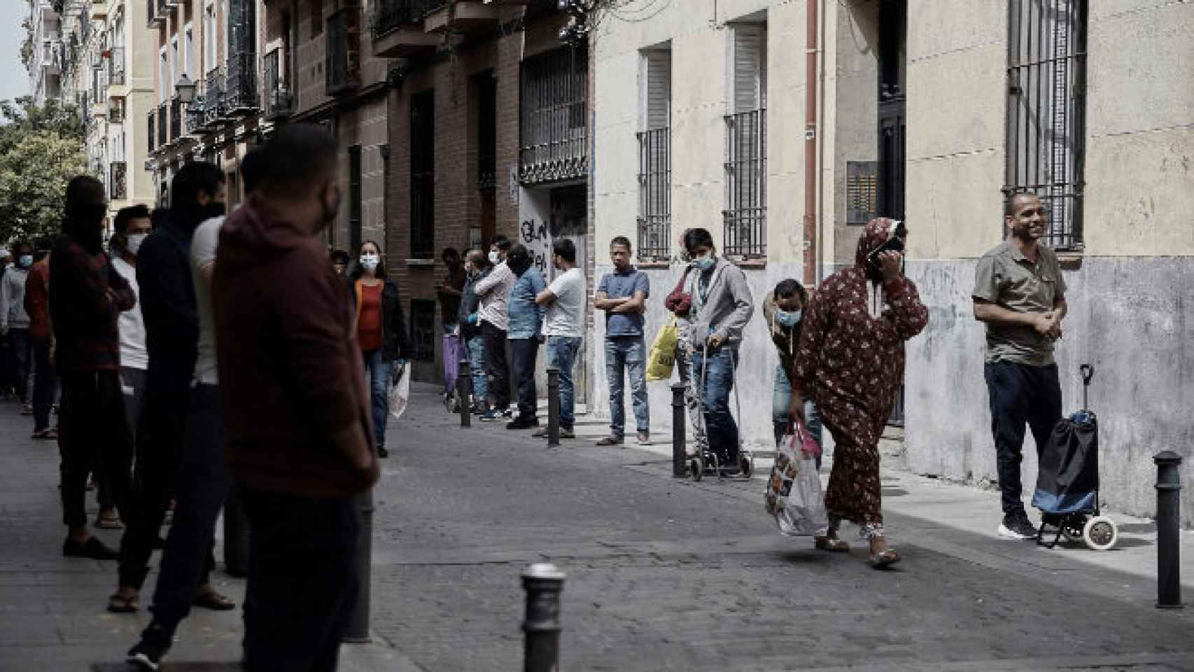 Varias personas hacen cola para recibir alimentos en el barrio madrileño de Lavapies.