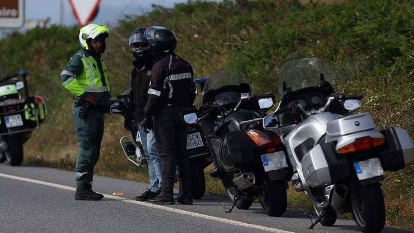 Un agente de la Guardia Civil dialoga con dos motociclistas que se han apeado de sus vehículos.