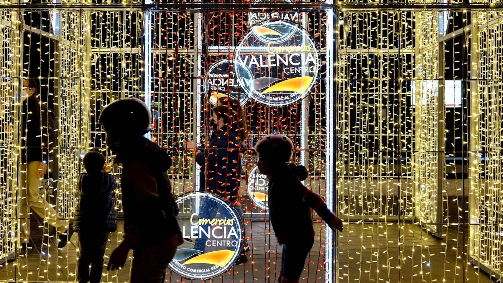 Unos niños juegan ante un cartel iluminado en el centro de Valencia.