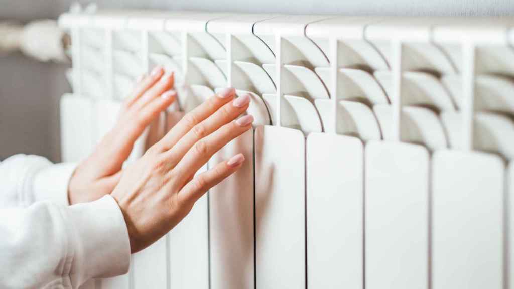 Una persona calienta sus manos en un radiador