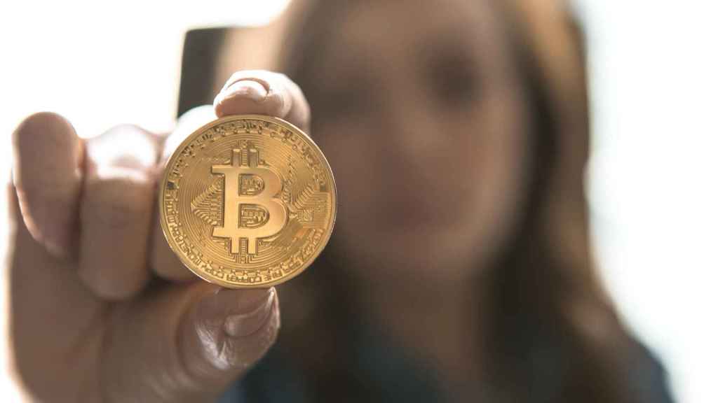 Una mujer sostiene una moneda física de bitcoin.