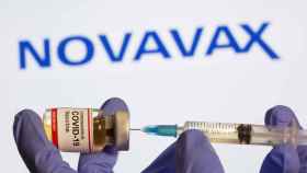 FILE PHOTO: A woman holds a small bottle labeled with a Coronavirus COVID-19 Vaccine sticker and a medical syringe in front of displayed Novavax logo in this illustration