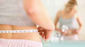 Una mujer mide la circunferencia de su cintura.