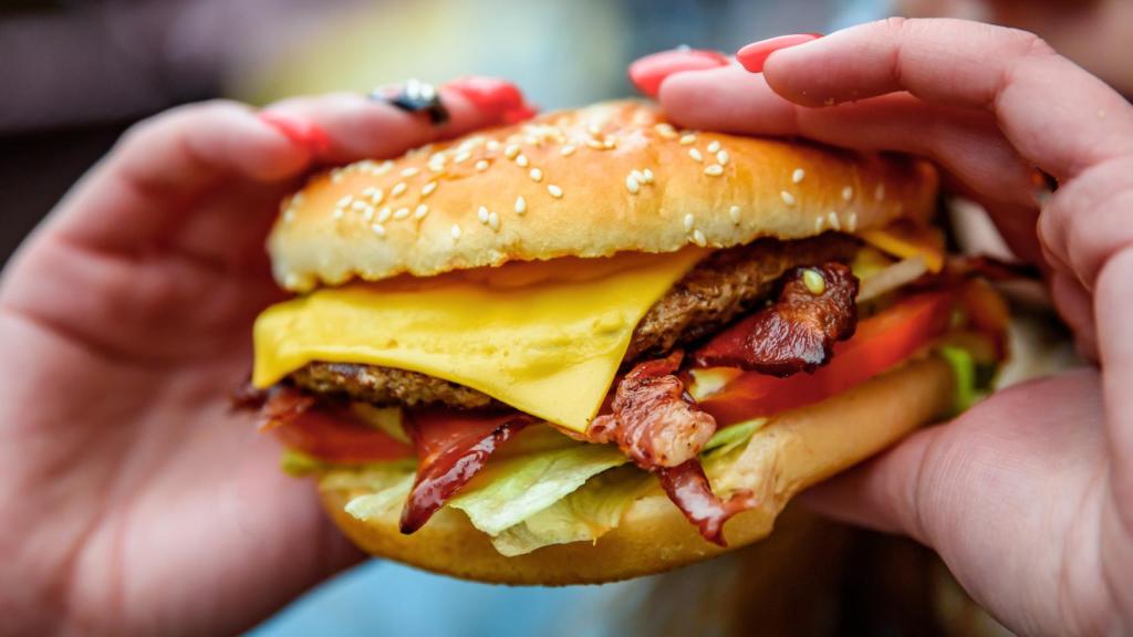 Una mujer sostiene una hamburguesa con muchos ingredientes.