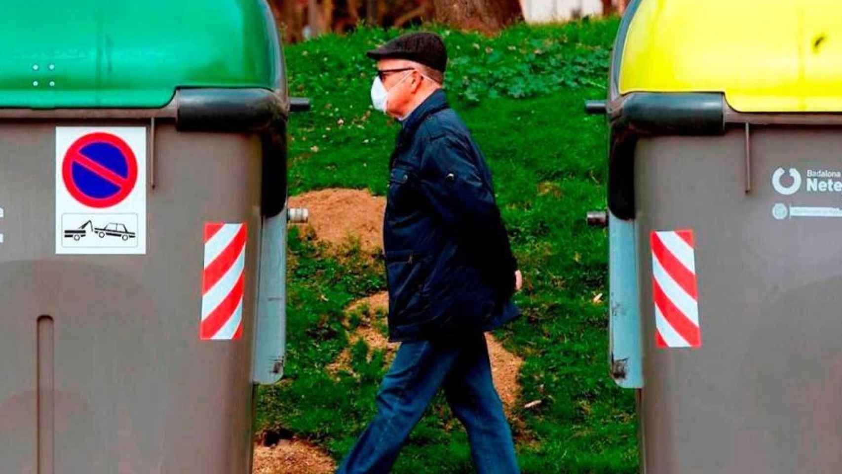 Un hombre camina entre dos contenedores de basura.