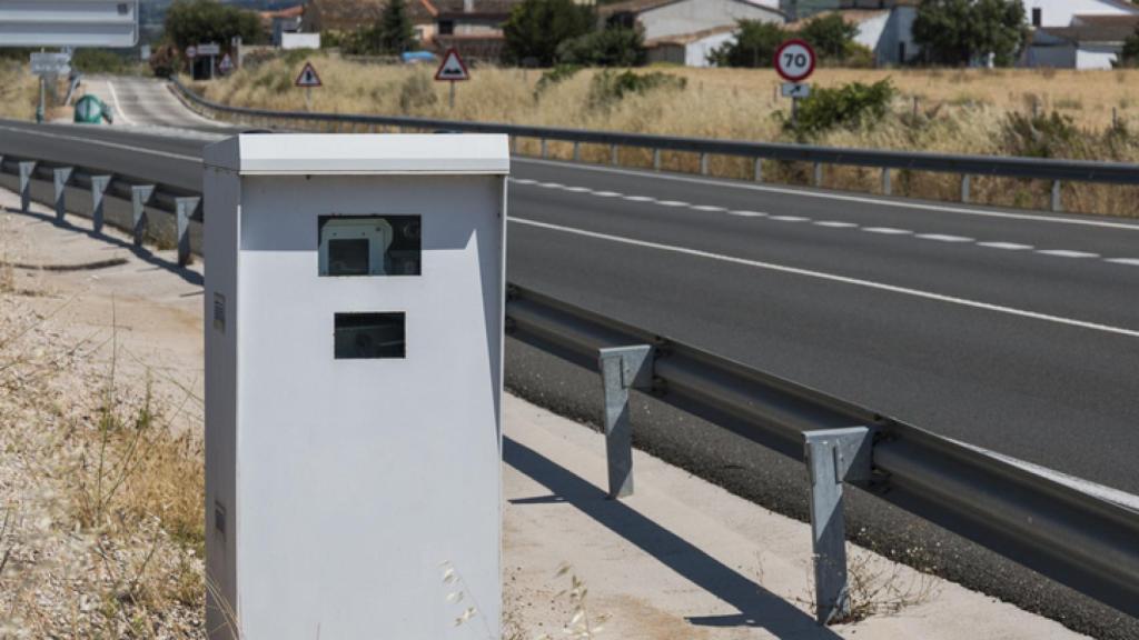 Un coche, en un autovía, pasando al lado de un radar de velocidad de la DGT.