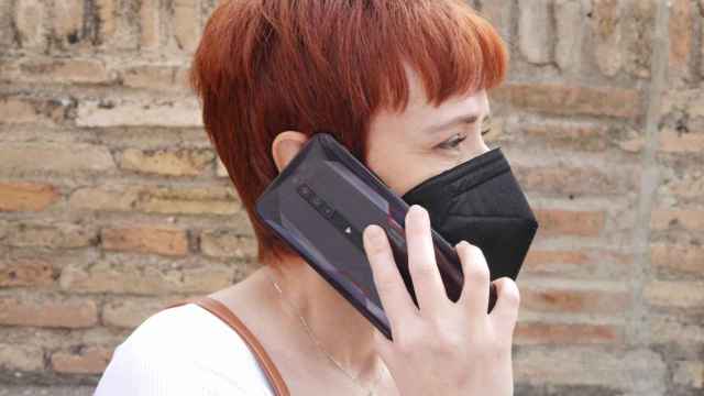 Una mujer con mascarilla hablando por su teléfono móvil.