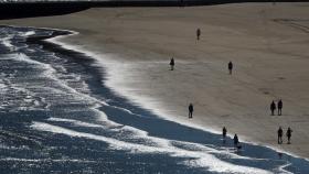 Varias personas pasean por la playa La Concha este viernes en la localidad cántabra de Suances.