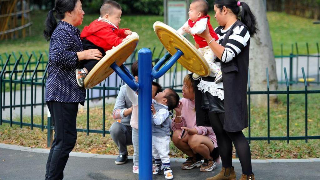 Tres mujeres juegan con varios niños pequeños en un parque.