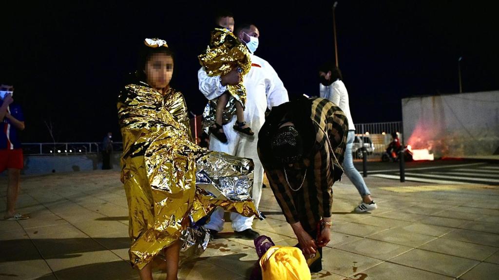 Un migrante coge en brazos a un menor acompañado de una mujer y una niña pequeña.