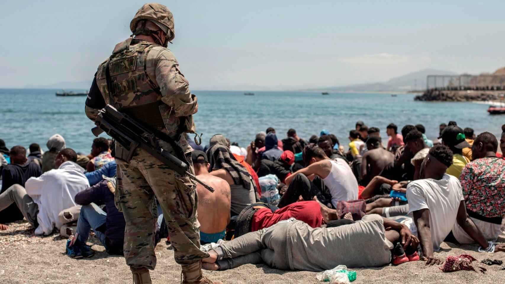 Inmigrantes sentados en la playa de El Tarajal, de Ceuta, ante un soldado español.