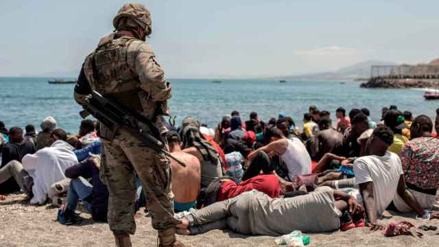 Inmigrantes sentados en la playa de El Tarajal, de Ceuta, ante un soldado español.