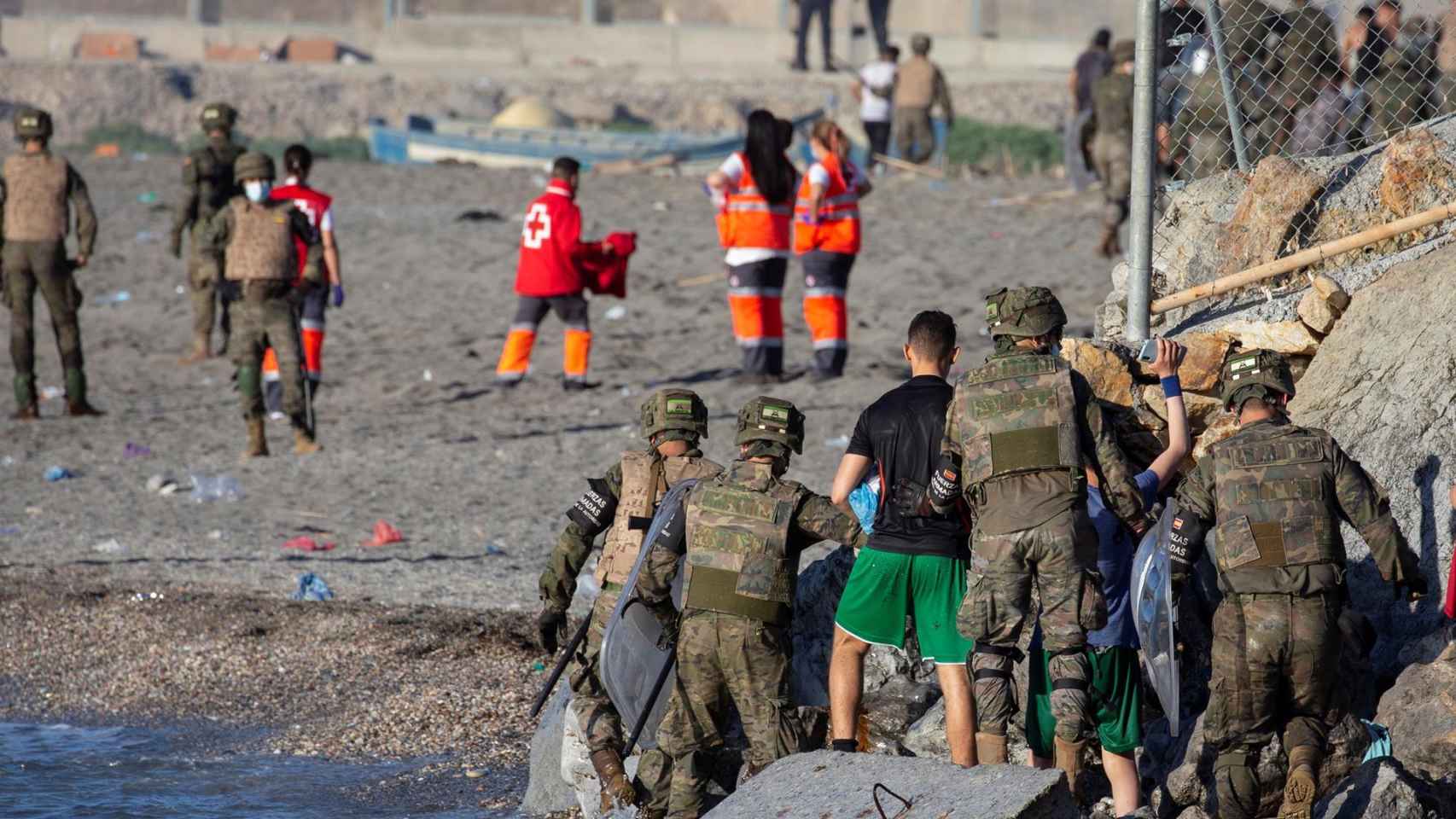 Miembros del Ejército ayudan a varios inmigrantes a su llegada a la playa de El Tarajal. Efe