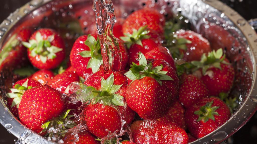 Un cuenco de fresas bajo un chorro de agua.