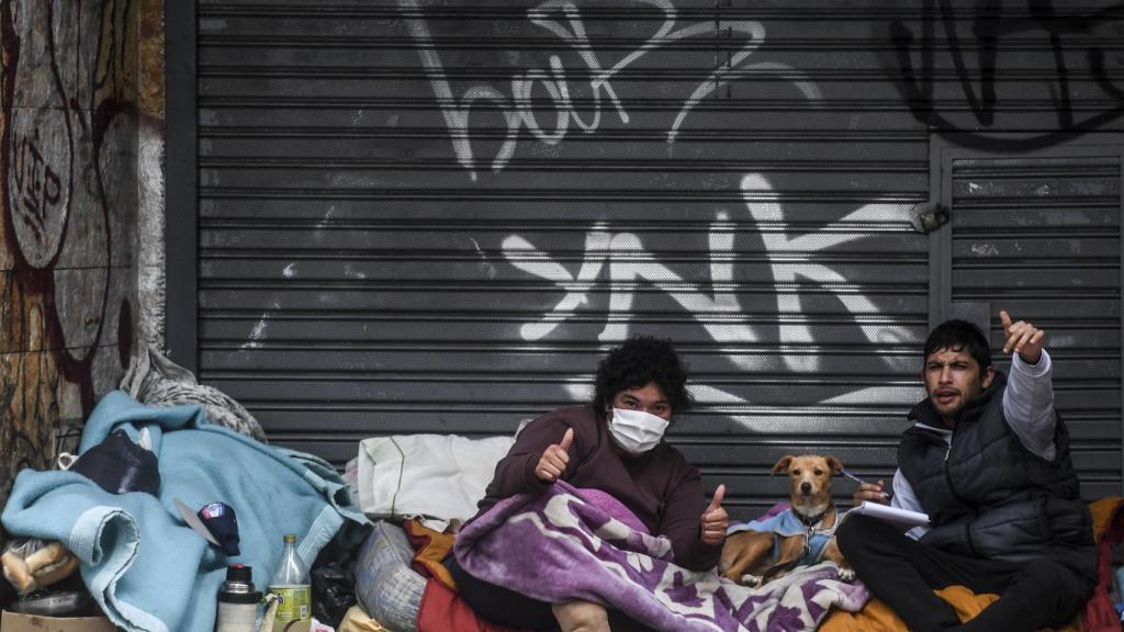 Dos personas que viven en la calle hacen gestos a la cámara.