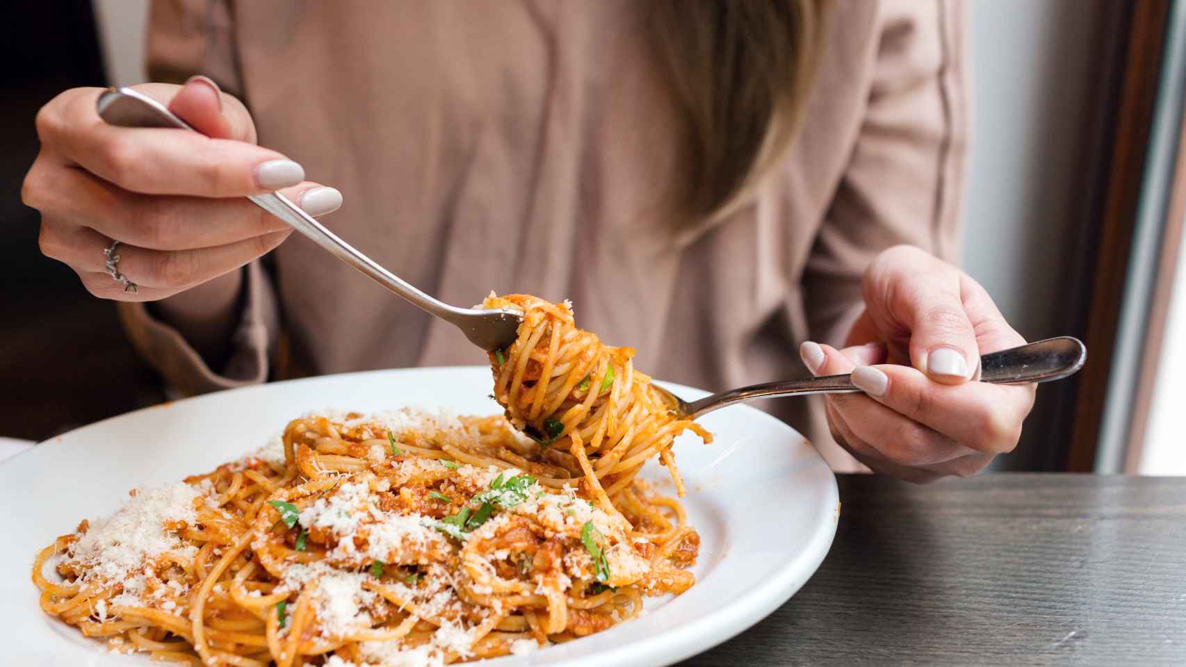 Una mujer come un plato de espaguetis con tomate y queso.