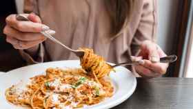 Una mujer come un plato de espaguetis con tomate y queso.