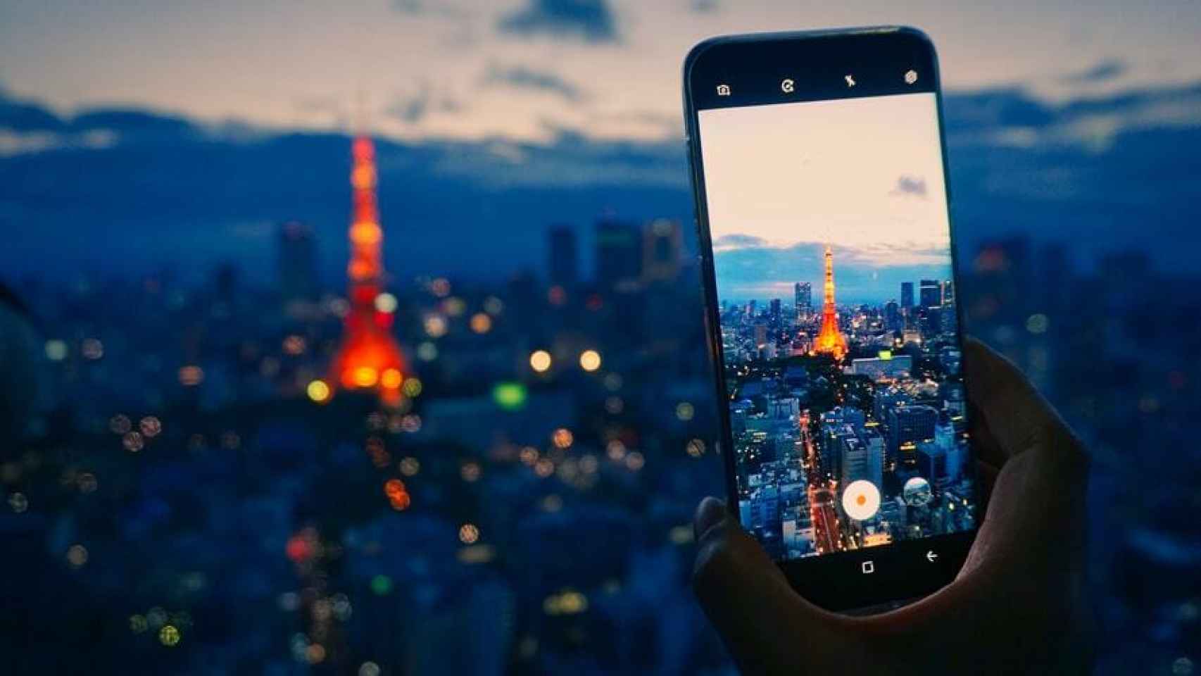 Un teléfono móvil fotografiando una torre en la distancia.