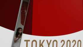 Una mujer se protege con su mascarilla cerca de un poster de los Juegos Olímpicos de Tokio 2020
