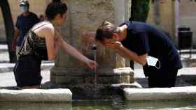 Varis personas se refrescan en una fuente de Córdoba para intentar sofocar las altas temperaturas.