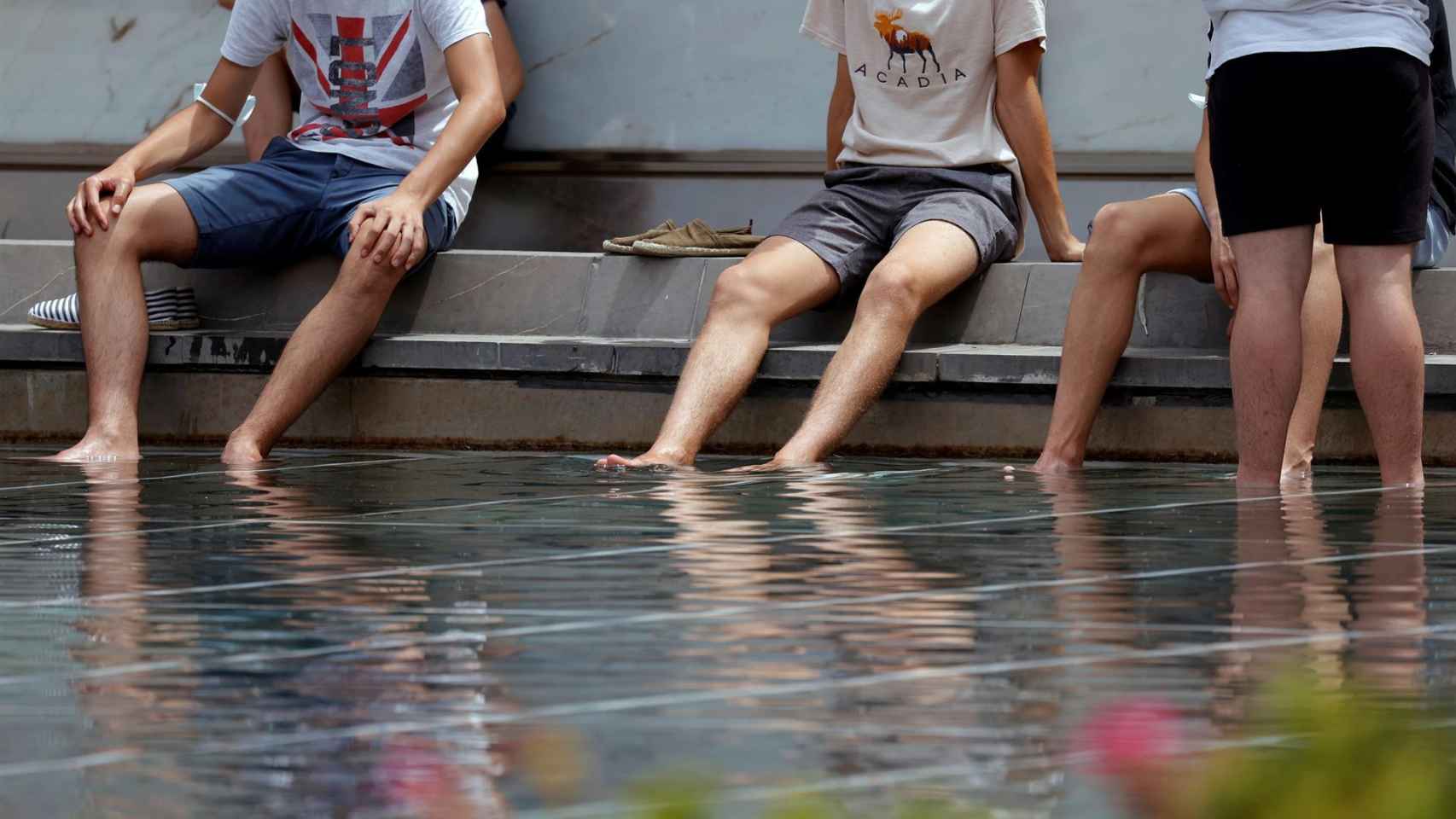 En la foto, un grupo de jóvenes se refrescan en un estanque.