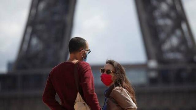 Dos jóvenes con mascarilla delante de la Torre Eiffel.