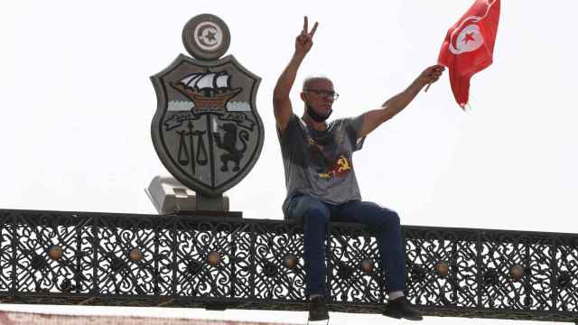 Un manifestante tunecino se sienta en la parte superior de una puerta fuera del edificio del parlamento en la capital del país.