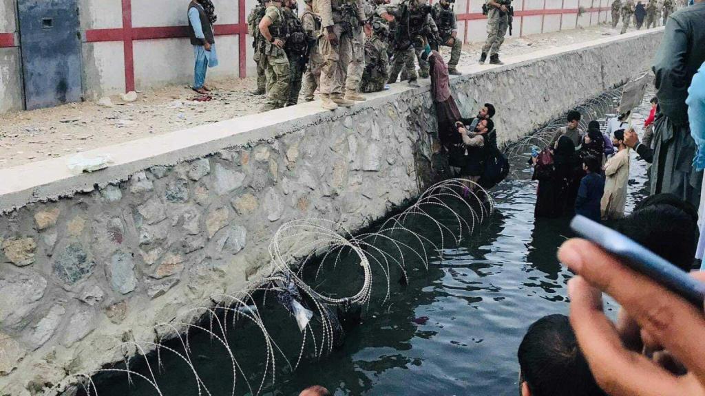 Varios afganos sortean el foto de agua que rodea un lateral del aeropuerto de Kabul, para huir del país.