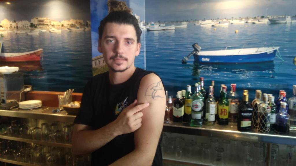 José Manuel, tras la barra del Restaurante La Cala, mostrando su tatuaje del Mar Menor y la Isla Rondella.
