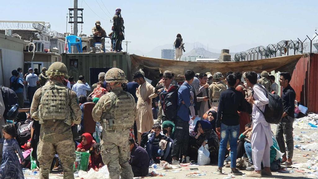 Two green berets before a group of Afghans at Kabul airport.  On top of the container, Taliban fighters.