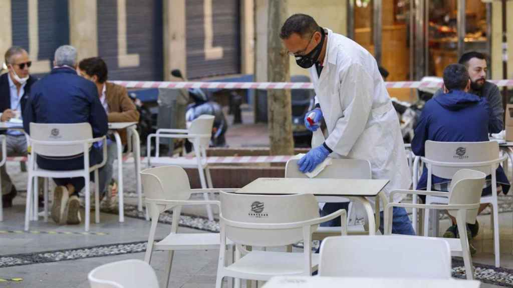 El trabajador de un bar limpia las sillas de una terraza, en Málaga.