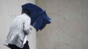 Un hombre se protege con un paraguas de la lluvia y el viento.
