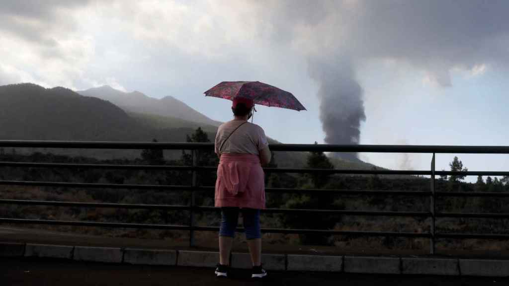 Una mujer, con un paraguas frente al volcán.