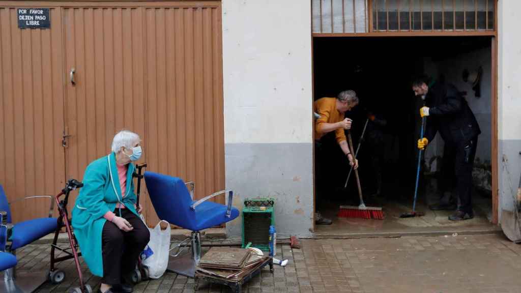 Una mujer observa a dos voluntarios achicando agua de su casa tras las inundaciones registradas en Villava, Navarra.
