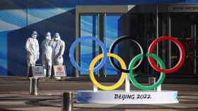 El logo de los Juegos Olímpicos de Invierno de Pekín 2022 junto a varios funcionarios protegidos con EPIs