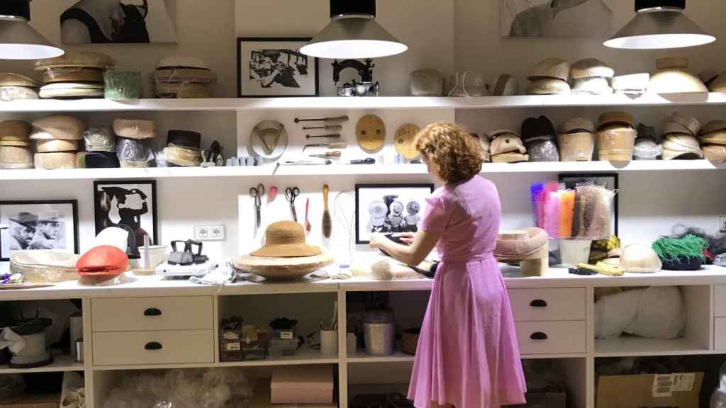 Una mujer observa varios sombreros en su taller de artesanía