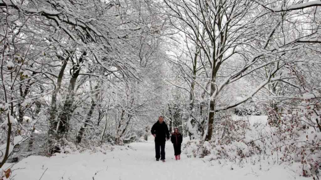 Imagen de un padre paseando con su hija en la nieve./