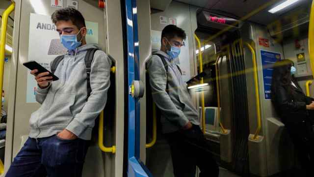 Un joven con mascarilla mira su teléfono móvil en el metro
