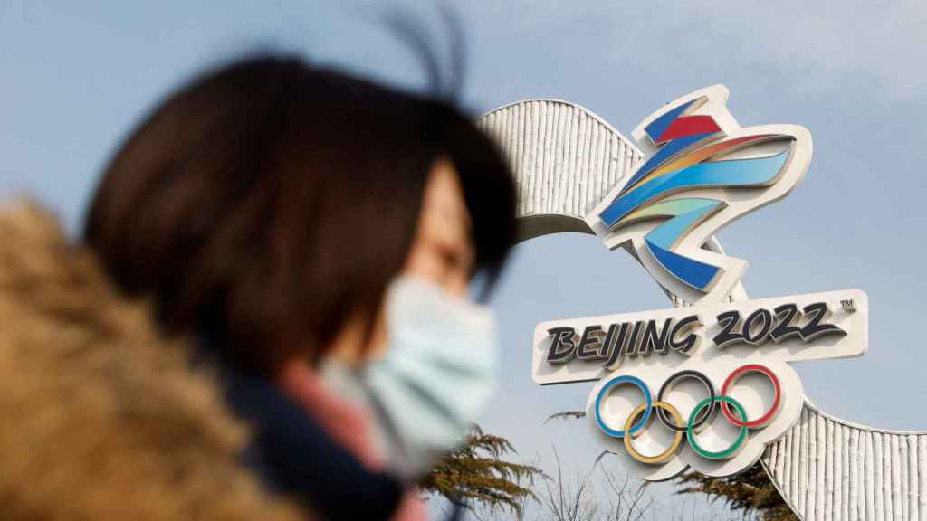 Una mujer camina enfrente del logo de Pekín 2022 en el óvalo de esquí nacional.