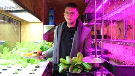 Lucas Cort, en el huerto de interior del restaurante El Hood, sujeta una bandeja con sus cultivos y elaboraciones y una hamburguesa.