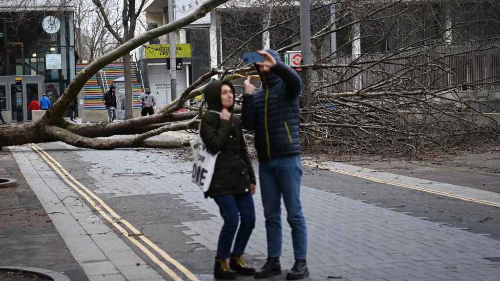 Dos personas se sacan una 'selfie' con un árbol caído detrás en Londres.
